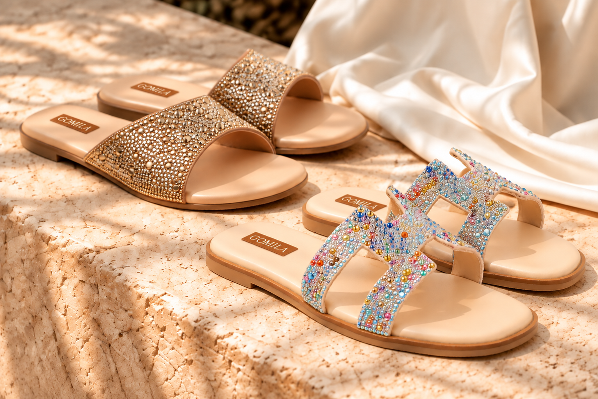 Tan buckle slides and crystal-strap flats on a sunlit stone ledge